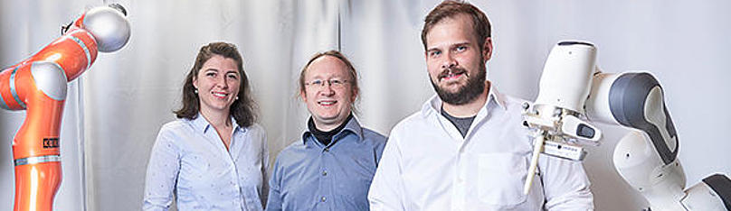 Jun.-Prof. Franziska Mathis-Ullrich, Prof. Björn Hein und Christian Kunz stehen neben Roboter, der Chirurgen bei der Bestimmung von Einstichstelle und -winkel unterstützt.