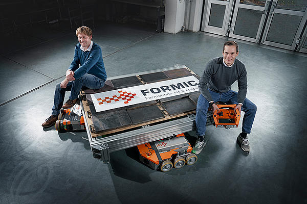 Dr.-Ing. Maximilian Hochstein und Dr.-Ing. Benedikt Klee sitzen auf FORMIC Transportsystem